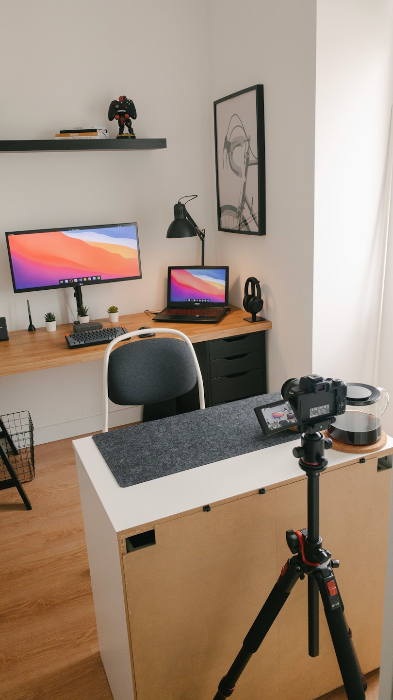 Schreibtisch mit Monitor, Laptop, Kamera und Kaffeekaraffe für die Content-Erstellung.