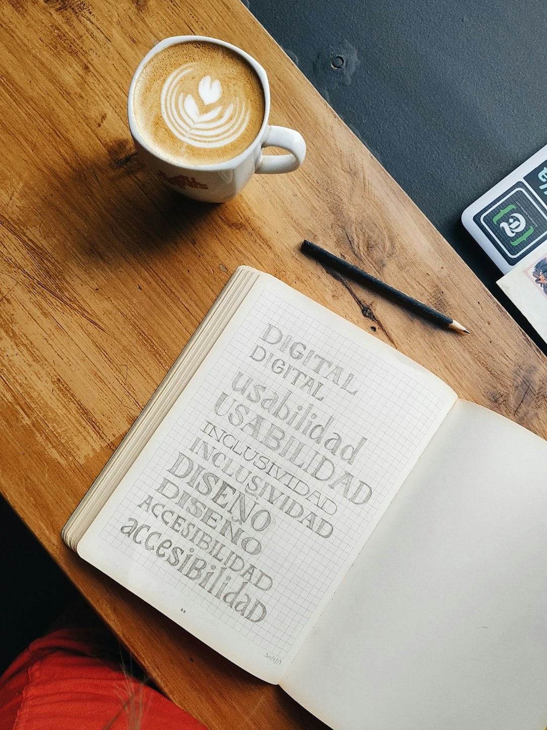 Notizbuch mit spanischen digitalen Design-Begriffen und Latte.