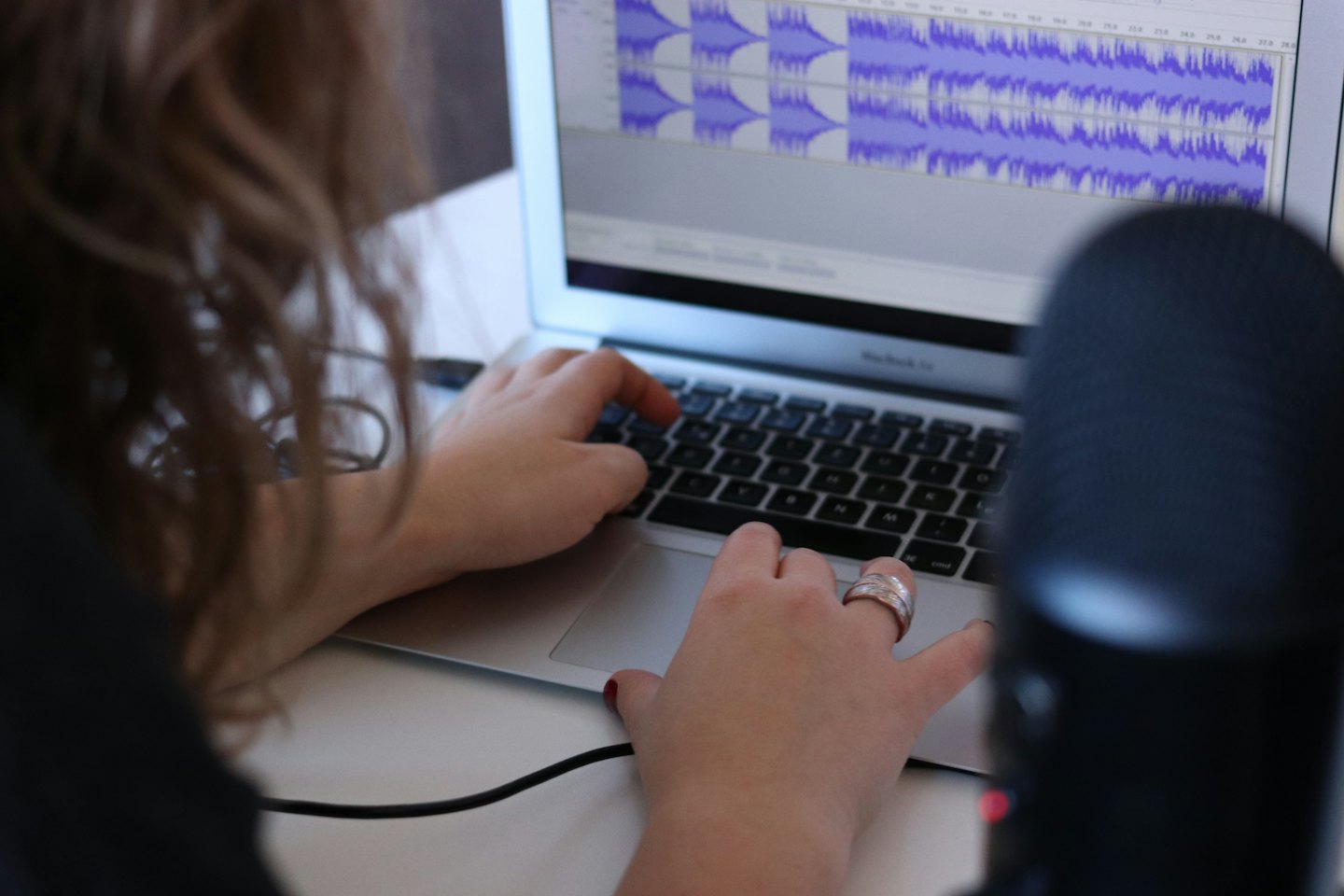 Person bearbeitet Audio auf einem Laptop mit Schallwellen auf dem Bildschirm.